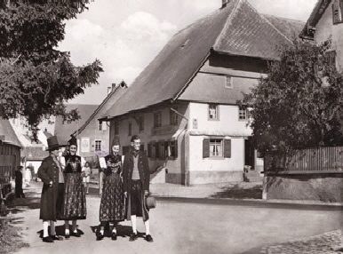 Historische Schwarz-Weiß-Aufnahme des Hauses mit Menschen in Tracht davor